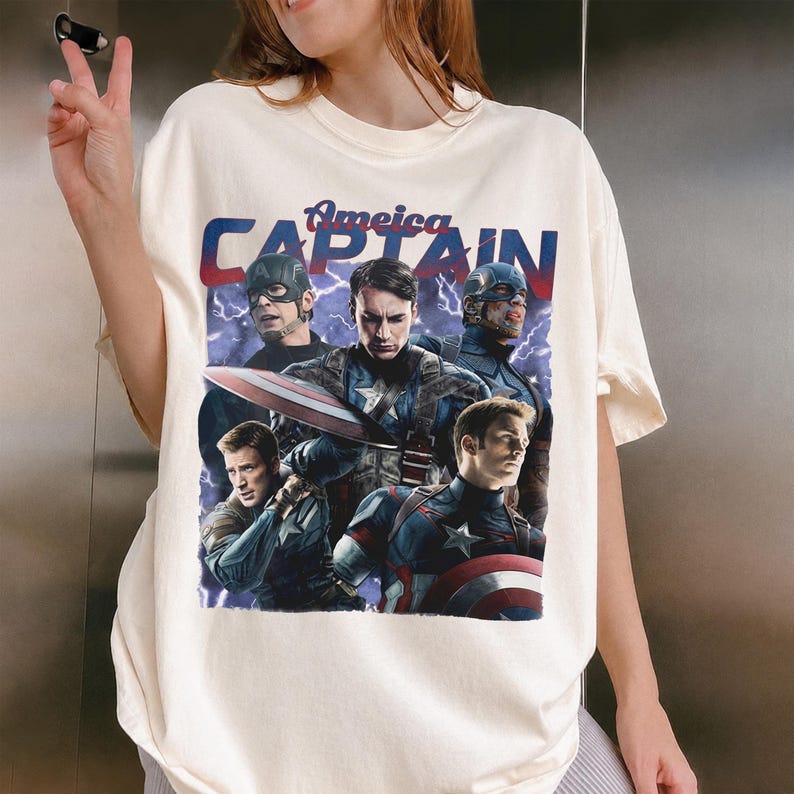 May include: Cream-colored t-shirt featuring a graphic of Captain America and the text "America Captain" in red and blue. The design includes multiple images of Captain America in various poses, with lightning bolts in the background.