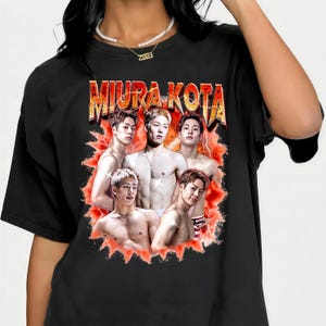 May include: Black t-shirt featuring a graphic of five shirtless men with the text "MIURA KOTA" in a gold and orange font. The graphic has a red and orange burst design around the men.