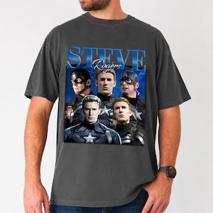 Op de afbeelding: Donkergrijze t-shirt met een afbeelding van Captain America met de tekst "STEVE Rogers" in blauw. De afbeelding toont meerdere afbeeldingen van het personage in verschillende poses. Het shirt is gemaakt van een zacht materiaal.