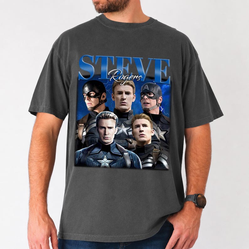 Op de afbeelding: Donkergrijze t-shirt met een afbeelding van Captain America met de tekst "STEVE Rogers" in blauw. De afbeelding toont meerdere afbeeldingen van het personage in verschillende poses. Het shirt is gemaakt van een zacht materiaal.