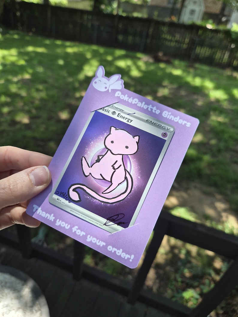 May include: A light purple card holder featuring a small white rabbit icon at the top, the text Pok&eacute;Palette Binders, and the text Thank you for your order! at the bottom. A psychic energy trading card with a pink Mew illustration is inserted inside.