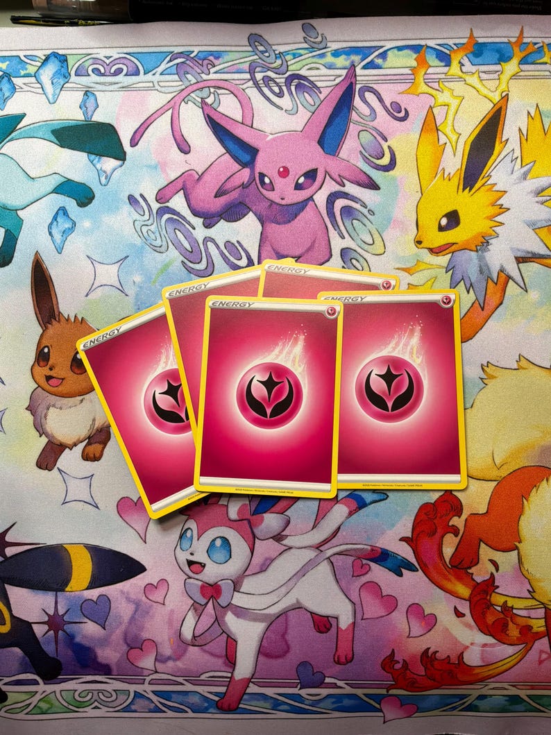 May include: Four pink Fairy-type energy trading cards from the Pok&eacute;mon card game. Each card features a central pink circular symbol with a black stylised star design surrounded by a white flame graphic, with the word ENERGY printed at the top.