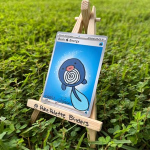 May include: A collectible trading card featuring a hand-drawn illustration of a blue Poliwag character on a Basic Water Energy card background, displayed on a small wooden easel with the text Poke Palette Binders written on the front rail.