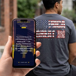 May include: A dark gray t-shirt with a large American flag design on the back, featuring the text "AMERICA THE GREAT" and a QR code. A smartphone displays a quote about resilience. The image is of a person from the back.