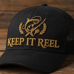 May include: A black baseball cap featuring gold embroidery on the front. The design includes a fishing rod and fish graphic above the text KEEP IT REEL. The cap has a structured front panel and a mesh back section for ventilation and a curved brim.