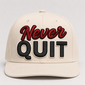 Puede incluir: Una gorra de béisbol de color beige con la palabra Never en una fuente cursiva roja y la palabra QUIT en letras de bloque negras y negritas. El texto está centrado en el panel frontal de la gorra, que tiene una corona estructurada y visera plana.