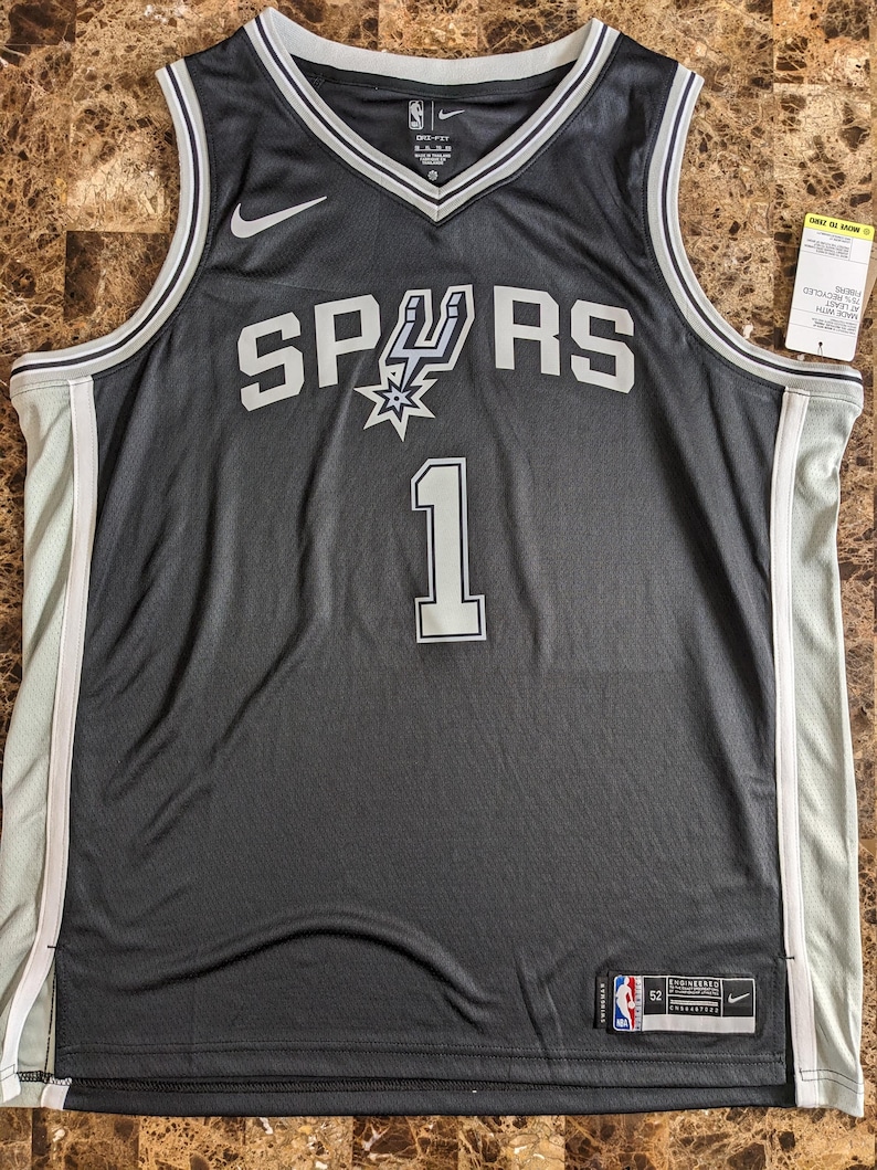 May include: A black San Antonio Spurs basketball jersey featuring the number 1 in white with grey trim. The jersey has a white Nike swoosh logo on the chest, a V-neck collar, and white side panels. A tag on the bottom left reads Engineered 52.