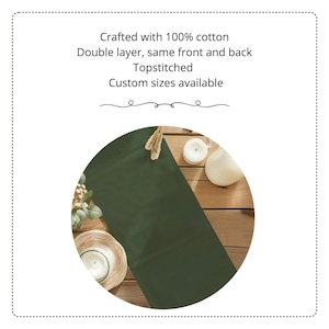K&ouml;nnte beinhalten: Ein dunkelolivgr&uuml;ner Tischl&auml;ufer aus 100% Baumwolle. Der Text lautet: Crafted with 100% cotton, Double layer, same front and back, Topstitched, Custom sizes available. Der L&auml;ufer liegt auf einer Holzoberfl&auml;che mit wei&szlig;en Kerzen.