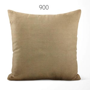 May include: A square throw pillow in a solid tan color with a smooth, uniform fabric texture. The number 900 is printed in a simple black sans-serif font centered above the pillow. The pillow has a standard square shape with rounded corners.