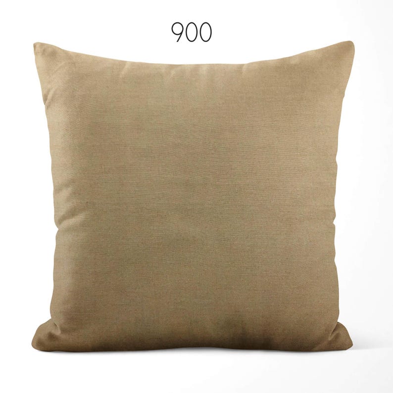 May include: A square throw pillow in a solid tan color with a smooth, uniform fabric texture. The number 900 is printed in a simple black sans-serif font centered above the pillow. The pillow has a standard square shape with rounded corners.