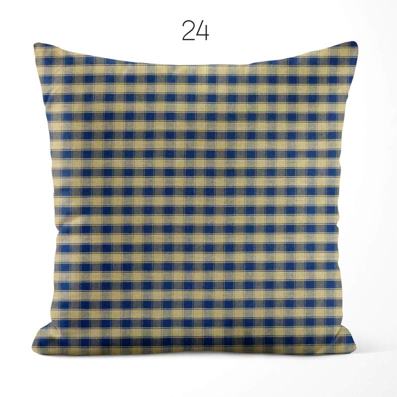 May include: A square throw pillow featuring a blue and beige checkered gingham pattern. The number 24 is printed in black above the pillow. The fabric has a visible woven texture throughout the design, creating a consistent grid of alternating colors.
