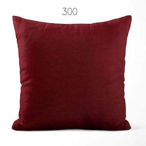 May include: A square throw pillow in a solid deep burgundy color with a smooth, matte texture. The number 300 is printed in a simple black sans-serif font centered above the pillow. The pillow has a standard square shape with pointed corners.