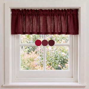 May include: A deep burgundy valance curtain with a gathered rod pocket top, hanging on a white window frame. The fabric has a visible woven texture. Three circular color swatches in shades of red and maroon are centered on the glass.