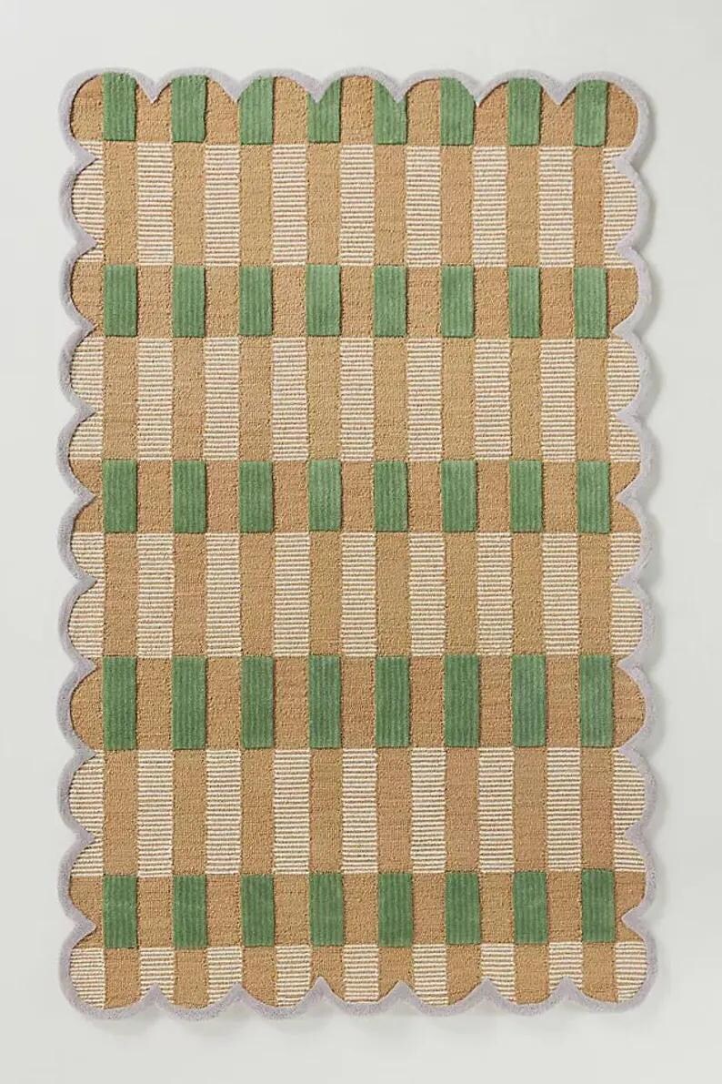 May include: A rectangular rug with a scalloped edge. The rug features a pattern of vertical stripes in tan and white, with green rectangular blocks. The border is a light grey colour.