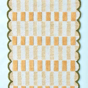 May include: A rectangular rug featuring a repeating pattern of vertical white and beige stripes, interspersed with beige rectangular blocks. The rug has a scalloped green border.