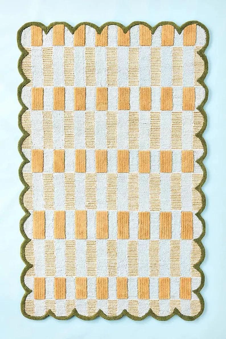 May include: A rectangular rug featuring a repeating pattern of vertical white and beige stripes, interspersed with beige rectangular blocks. The rug has a scalloped green border.