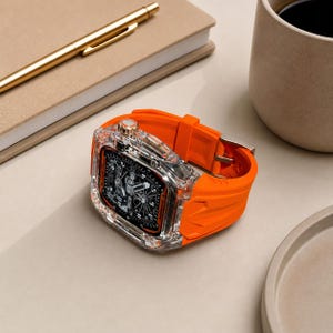 Puede incluir: Un reloj transparente con una correa naranja y una esfera negra. El reloj tiene una corona dorada y un cierre plateado. El reloj está sobre una superficie clara, junto a un cuaderno, un bolígrafo y una taza de café.