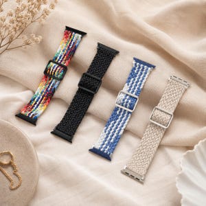 Puede incluir: Cuatro correas de reloj trenzadas en varios colores. Una correa es multicolor, otra negra, otra azul y blanca, y la última beige. Cada correa tiene una hebilla y conectores.