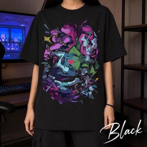 Könnte beinhalten: Ein schwarzes Kurzarm-T-Shirt mit einem lebendigen Grafikdruck von drei stilisierten Charakteren in Violett-, Grün- und Blautönen. Das Design enthält ein zentrales rotes Herzsymbol sowie dynamische, kantige Formen auf schwarzem Grund.