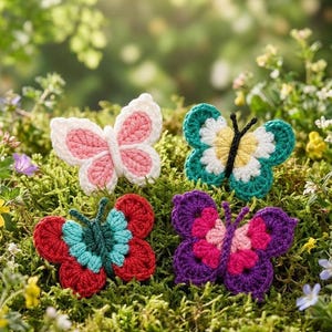 May include: Four colorful crochet butterflies rest on a bed of green moss. The butterflies are in shades of pink, red, teal, green, and purple. Each butterfly has a unique pattern and color combination, with detailed wing designs.