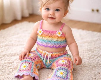 May include: A baby wearing a handmade crochet outfit. The outfit includes a rainbow-colored crop top and matching pants, both adorned with daisy accents. The baby has blonde hair styled in pigtails, each with a daisy hair accessory.