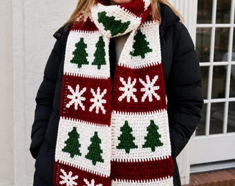 May include: A long crochet scarf featuring a repeating pattern of dark green pine trees on a cream background and white snowflakes on a deep red background. The scarf is constructed with alternating blocks of these festive colors and designs.