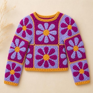 Op de afbeelding: Een gehaakte trui met lange mouwen, opgebouwd uit vierkante panelen met een herhalend bloemmotief. Het ontwerp toont een levendig kleurenpalet van diep magenta, licht lavendel en heldergeel, met een gele rand bij de halslijn.