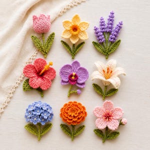 May include: A collection of nine crocheted flower appliques arranged in a grid. The set includes a pink tulip, yellow daffodil, purple lavender, red hibiscus, purple orchid, white lily, blue hydrangea, orange marigold, and a light pink cherry blossom.
