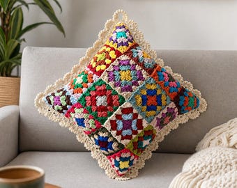 May include: A square crochet pillow cover featuring a vibrant granny square pattern in multiple colors including red, blue, yellow, green, and purple. The pillow is finished with a cream-colored scalloped crochet border and a small hanging loop.