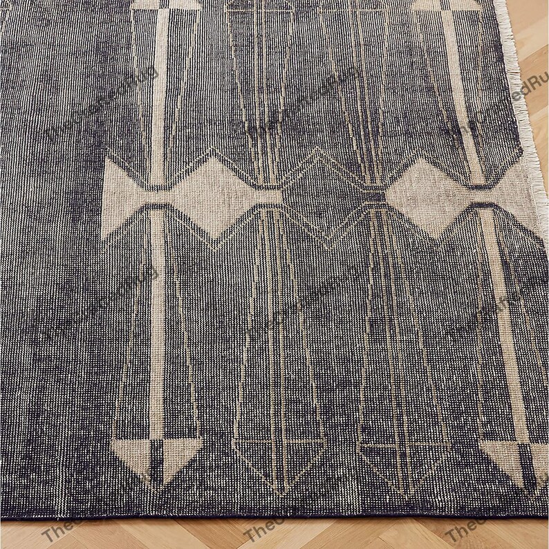 May include: A close-up of a navy blue and beige patterned rug. The rug features a geometric design with vertical and horizontal lines, and diamond and arrow shapes. The rug has a textured appearance and a fringed edge.