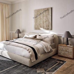 May include: A bedroom scene featuring a large bed with a textured, light-colored base and a layered white and beige comforter. A dark gray rug with geometric patterns sits at the foot of the bed. Two bedside tables with lamps and a large abstract painting complete the room.