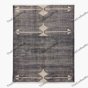 May include: A rectangular, dark gray rug with a geometric pattern. The design features diamond and arrow shapes in a lighter beige color, creating a contrasting visual effect. The rug has a fringe along the top edge, adding a textured detail.