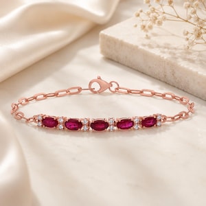 Pode incluir: Uma pulseira de corrente em ouro rosa com cinco pedras preciosas vermelho-escuras de corte oval alternadas com pequenas pedras claras. A pulseira inclui um fecho lagosta e uma série de elos ovais que ligam a cravação central ao fecho.