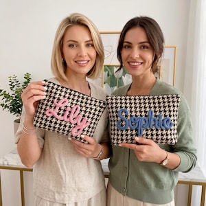 May include: Two rectangular zippered pouches featuring a black and white houndstooth pattern. One pouch displays the name Lily in raised pink script lettering, while the other displays the name Sophie in raised blue script lettering.