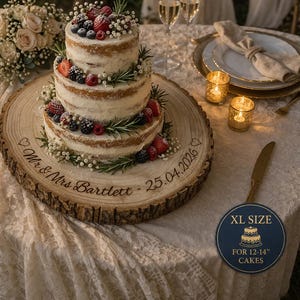 May include: A three-tiered wedding cake decorated with berries and rosemary sits on a wooden cake stand. The stand is engraved with "Mr & Mrs Bartlett 25.04.2026". The cake is on a table with candles and champagne glasses.