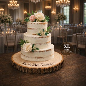 May include: A three-tier naked wedding cake decorated with white and pink roses and green leaves, resting on a round wooden log slice stand engraved with the text Mr. & Mrs. Davies and a heart. A circular badge indicates XL size up to 14" cake.