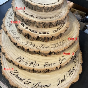May include: A stack of five circular wooden tree slices with natural bark edges, each engraved with names and dates in various fonts labeled Font 1, 3, 4, 5, and 6. The engravings include Mr & Mrs Thompson, Tomlinson, Snow, Pyke, Robson-Bell, and David & Leanne.