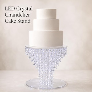 Könnte beinhalten: Ein LED-Kristall-Kronleuchter-Kuchenständer, der einen dreistöckigen weißen Kuchen trägt. Der Ständer hat eine transparente, kreisförmige Basis und eine mit Kristallen verzierte Plattform. Der Text "LED Crystal Chandelier Cake Stand" ist sichtbar.