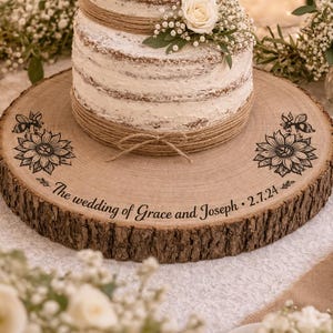 Peut inclure: Un présentoir à gâteau en bois rustique avec un bord en écorce, sur lequel repose un gâteau à plusieurs niveaux orné de fleurs et de ficelle. Le présentoir porte l'inscription "The wedding of Grace and Joseph - 2.7.24" et des motifs floraux.
