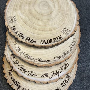 May include: A stack of four circular wooden slices with natural bark edges, each engraved with custom text and dates. The top slice features floral designs and the text Mr & Mrs Prior 06.08.2026. Other slices display names and dates including Mr & Mrs Johnson, Mr & Mrs Tarr, and The wedding of Danielle and Jamie.