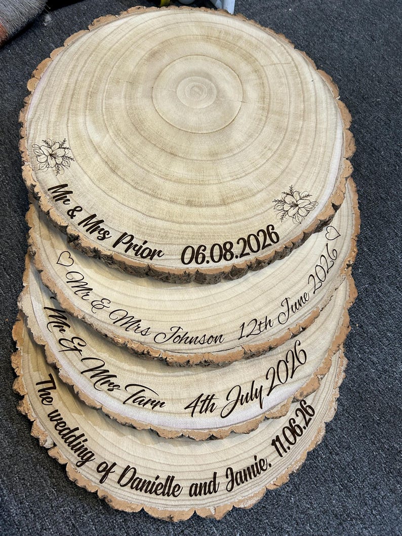 May include: A stack of four circular wooden slices with natural bark edges, each engraved with custom text and dates. The top slice features floral designs and the text Mr & Mrs Prior 06.08.2026. Other slices display names and dates including Mr & Mrs Johnson, Mr & Mrs Tarr, and The wedding of Danielle and Jamie.