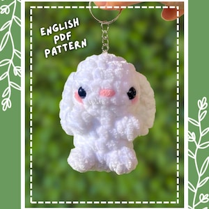 May include: A white crocheted baby bunny keychain with black eyes and pink cheeks, attached to a silver metal ring. The image includes the text "baby bunny keychain", "ENGLISH PDF PATTERN", and "XENcrochet" on a green background with white leaf outlines.