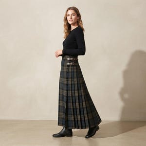 以下が含まれることがあります： ダークグリーン、ブルー、ブラウンのタータンチェック柄が特徴のロング丈プリーツスカート。ウエスト部分には、シルバーカラーの金属製バックルが付いた2本の調節可能なレザーストラップがあしらわれています。シンプルな黒の長袖トップスと組み合わせています。