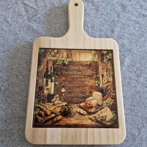 May include: Wooden chopping board with a handle, featuring a printed image of a wine-themed still life. The image includes wine bottles, glasses, cheese, and the text "Recipe for a Perfect Wine Night."