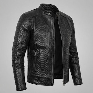 Könnte beinhalten: Eine schwarze Jacke mit einem strukturierten Schlangenledermuster auf der gesamten Außenseite. Das Kleidungsstück verfügt über einen Stehkragen mit Druckknopfverschluss, einen durchgehenden Frontreißverschluss und zwei vertikale Reißverschlusstaschen.