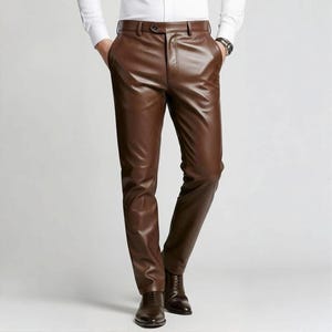 Puede incluir: Pantalones de cuero marrón con cinturón y cierre de botón. Los pantalones tienen un corte clásico y a medida y se combinan con zapatos de vestir marrones. El cuero tiene un acabado liso y brillante, y los pantalones tienen bolsillos.