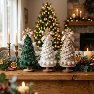 May include: Three cone-shaped crochet Christmas trees in dark green, white, and beige. Each tree features a textured bobble stitch pattern, a gold-colored star topper, and a beige satin ribbon bow. The trees stand on small wooden pedestals.