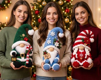 May include: Three handmade crochet gnomes featuring festive designs. The left gnome is green with a lantern and candy cane. The center gnome is blue with a snowflake hat and a sign reading Let it Snow. The right gnome is red and white striped.