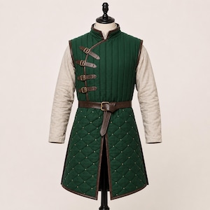 May include: A dark green quilted waistcoat featuring a high collar and long beige sleeves. The garment has four brown leather straps with metal buckles on the upper chest and a brown leather belt at the waist. The lower section has a diamond pattern.