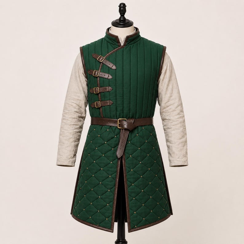May include: A dark green quilted waistcoat featuring a high collar and long beige sleeves. The garment has four brown leather straps with metal buckles on the upper chest and a brown leather belt at the waist. The lower section has a diamond pattern.
